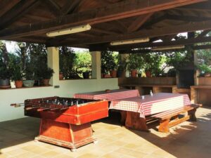 Zona de barbacoa exterior cubierta con mesas para grupos y futbolín en la casa rural Can Micós, Girona.