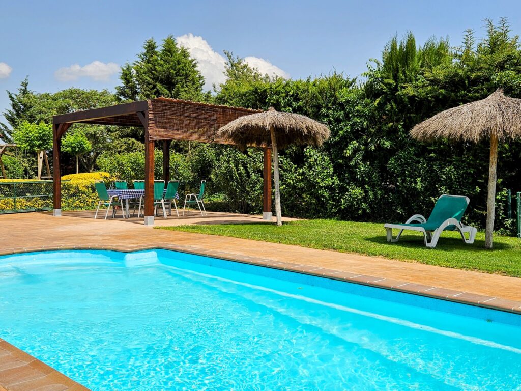 Private swimming pool area with straw umbrellas and a wooden pergola at Can Micos villa in Girona, Spain.