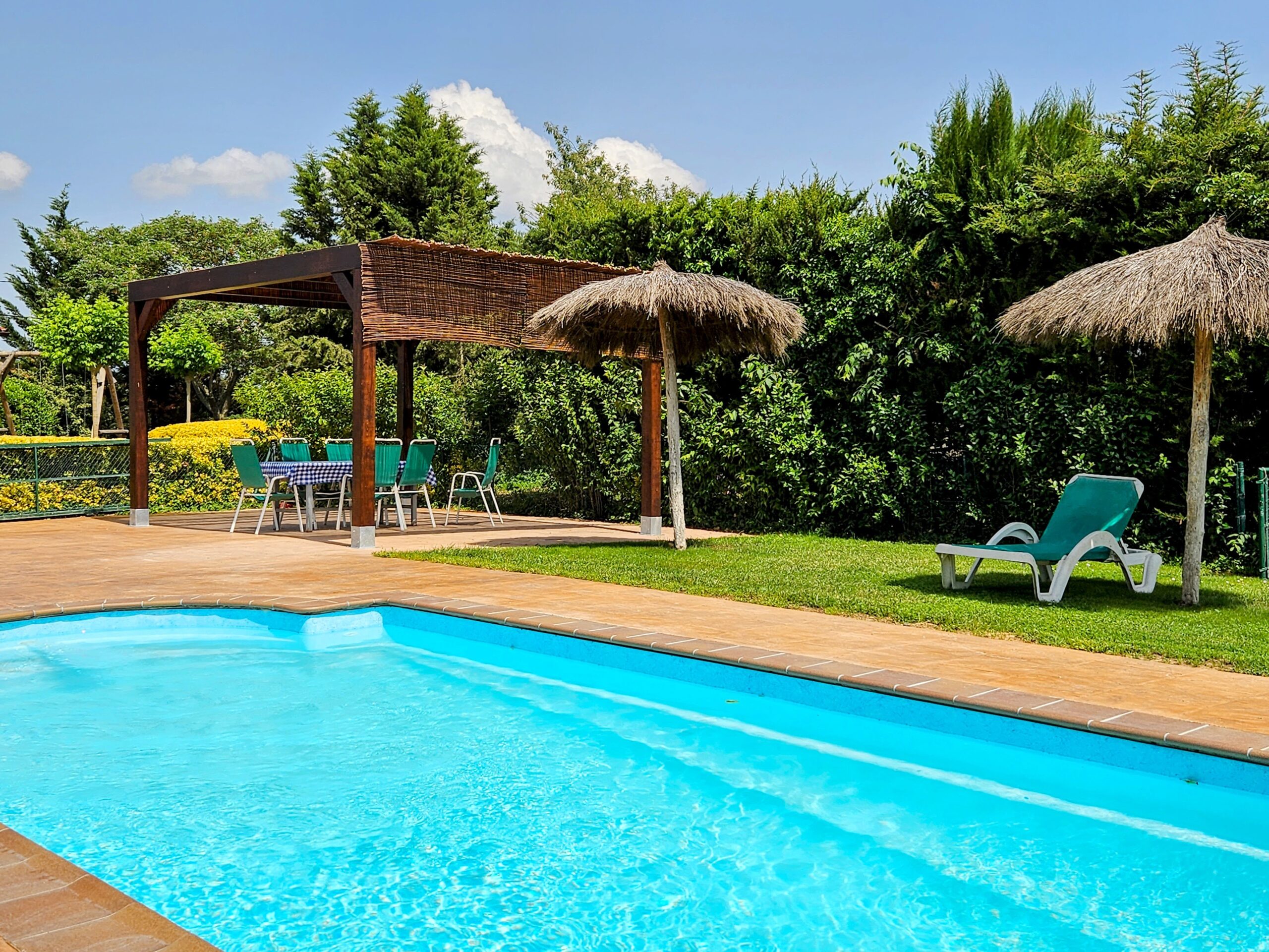 Piscine avec parasols en paille et pergola en canisse dans le jardin du mas Can Micos, idéale pour des vacances à Gérone.